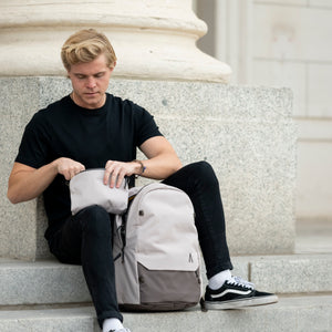 A man inspects his belongings while he sits next to a granite column with his Boundary Supply backpack.