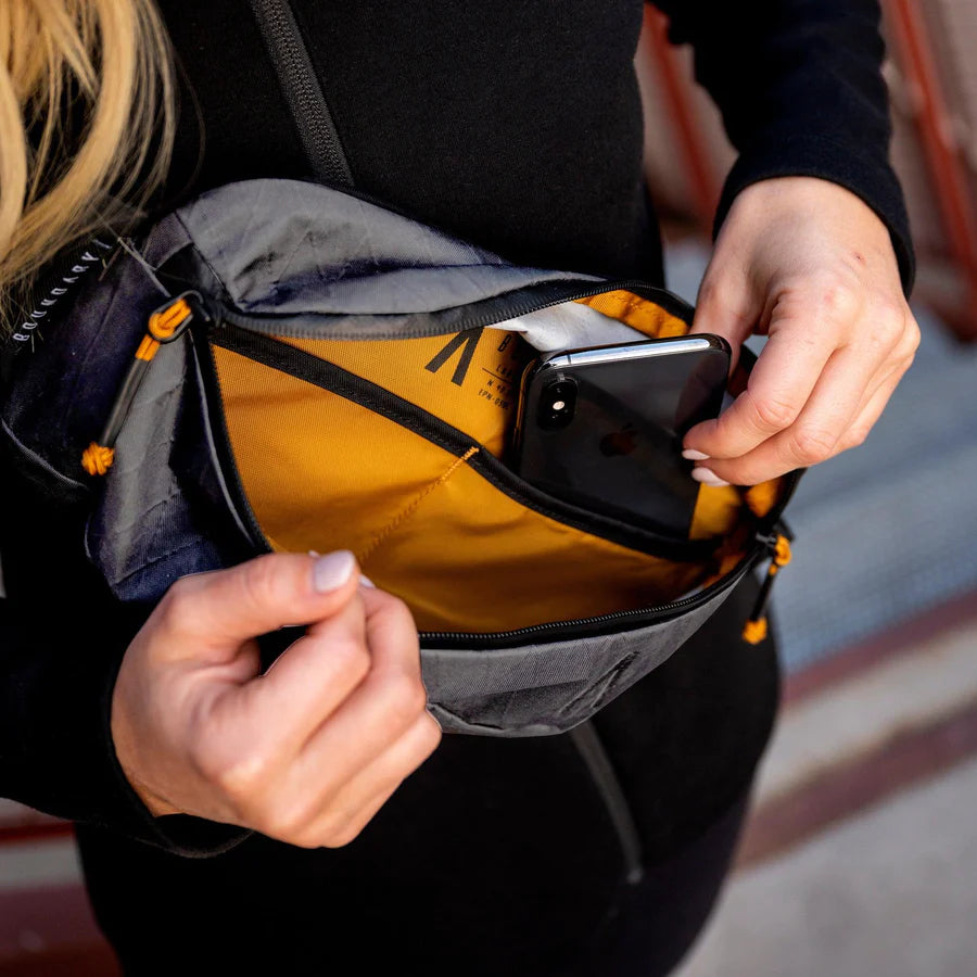 Woman putting her phone inside her yellow and gray Rennen X-Pac Crossbody